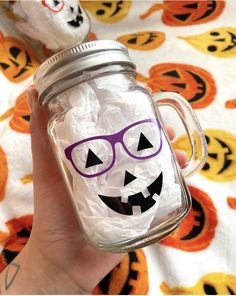 a hand holding a mason jar filled with white paper and plastic wrap, decorated like a jack - o'- lantern