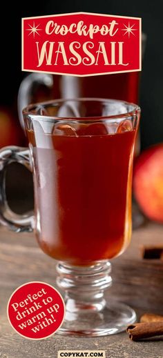 a cup of crockpot wassail on a table with cinnamon sticks and an apple in the background