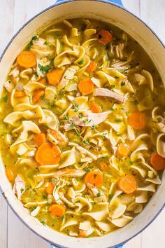 a pot filled with chicken noodle soup on top of a white wooden table next to a spoon