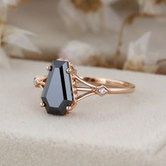 a black diamond ring sitting on top of a white cloth covered box with flowers in the background