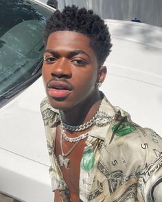 a young man with his tongue out sitting in front of a white car wearing a necklace