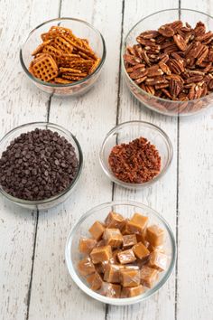 four glass bowls filled with different types of chocolate and pretzel snack toppings