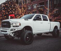 a white ram truck parked in front of a building with christmas lights on the trees