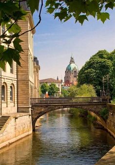 a bridge over a river with buildings in the back ground and trees on either side