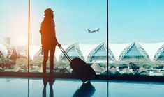 a woman is standing in an airport with her luggage and looking out the window at planes