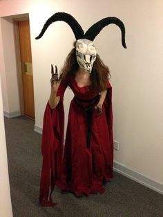 a woman in a red dress holding two knives and wearing a goat mask with horns on her head