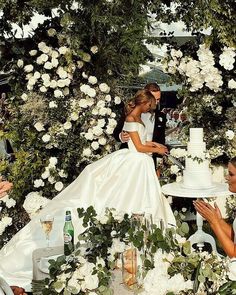 a bride and groom are cutting their wedding cake at the table surrounded by white flowers