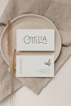 two business cards sitting on top of a white plate next to a dried grass plant