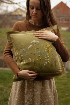 a woman holding a green pillow with flowers on it