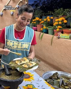 a woman in an apron is serving food from a bowl on a table with flowers and potted plants