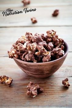 a wooden bowl filled with chocolate covered candies on top of a wooden table next to pieces of walnuts