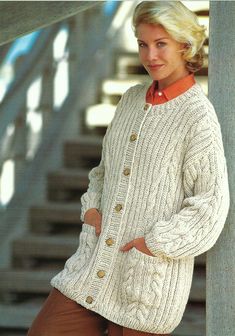 a woman wearing a white sweater and brown pants standing next to a stair case with her hands on her hips