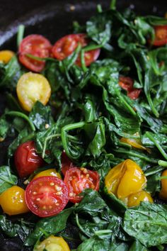 spinach, tomatoes and other vegetables are cooking in a skillet on the stove