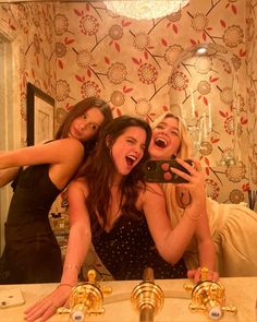 three women taking a selfie in front of a bathroom mirror with gold faucets