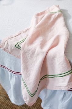 an unmade bed with pink linens and green piping on the bottom half