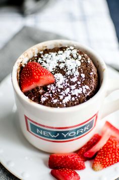 a chocolate mug cake with powdered sugar and strawberries on the side sitting on a plate