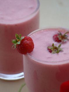 two glasses filled with pink smoothie and strawberries