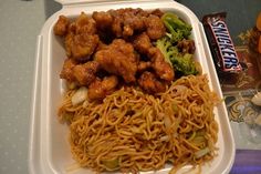 a plastic container filled with noodles, meat and veggies next to a candy bar