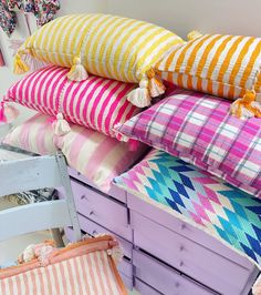 a stack of colorful pillows sitting on top of a wooden dresser next to a chair