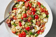 a white bowl filled with pasta salad topped with tomatoes, cucumbers and parsley