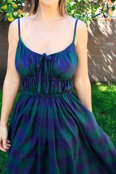 a woman standing in the grass wearing a blue and green dress with an orange tree behind her