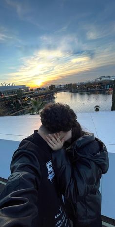 a man is covering his face with his hands while looking at the sunset over a body of water