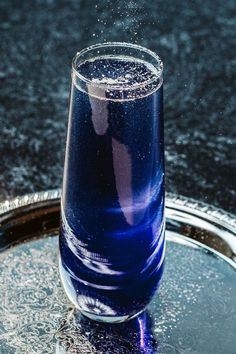 a blue liquid in a glass on top of a silver tray with water splashing out of it