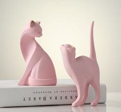 two pink cat figurines sitting on top of a book