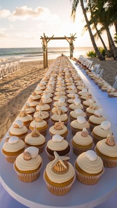 cupcakes are lined up on a long table at the beach for a wedding