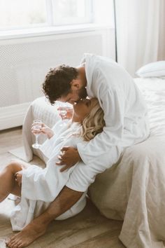 a man and woman kissing while sitting on the floor in front of a white bed