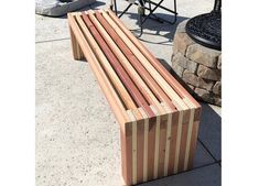 a wooden bench sitting on top of a sidewalk next to a stone wall and fire pit