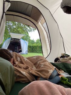 a woman laying in a tent with her head on the pillow and sleeping under a blanket