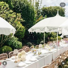 a long table with white umbrellas and flowers on it is set for an outdoor dinner