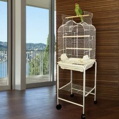 a green bird sitting on top of a white birdcage next to a window