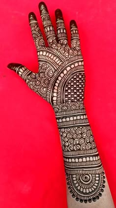 a hand with henna on it is shown against a red background and has an intricate pattern