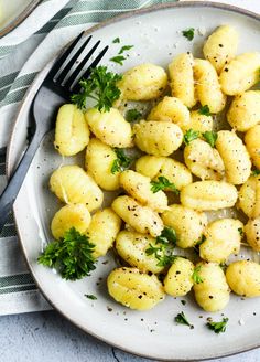 a white plate topped with gnocchini and parsley next to a fork