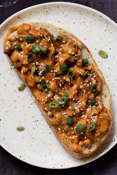 a piece of bread with sauce and green onions on it sitting on a white plate