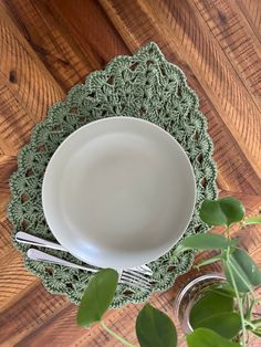 a white plate and silverware on a green doily next to a potted plant