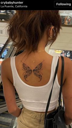 a woman with a butterfly tattoo on her back is looking down an escalator