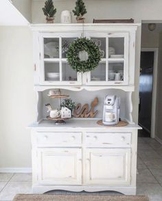 a white hutch with christmas wreath on top and coffee maker in the bottom right corner