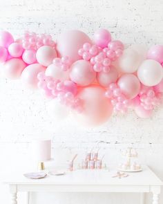 a white table topped with lots of pink balloons next to a white brick wall filled with confetti