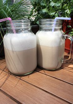 two mason jars filled with milk sitting on top of a wooden table next to plants