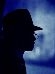 the silhouette of a man wearing a hat in front of a blue wall with light coming through it