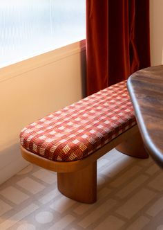 a wooden bench sitting in front of a window next to a red and white checkered table cloth