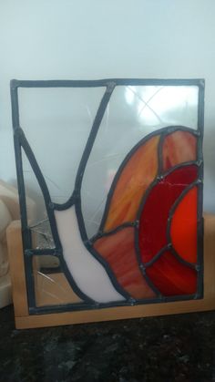 a stained glass window sitting on top of a wooden stand next to a white vase