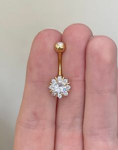 a person's hand holding a gold nose ring with a flower design on it