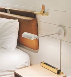 a bed with white sheets and a wooden headboard on the wall next to a lamp