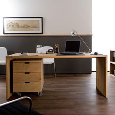 a desk with a laptop on it in an office space next to a chair and window