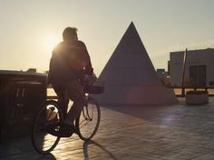 the man is riding his bike on the sidewalk in front of some pyramid shaped structures