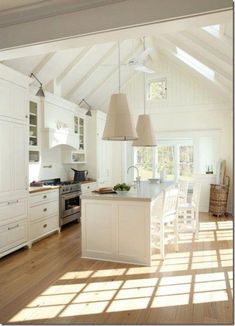 an open kitchen and dining room with white cabinets, wood flooring and large windows